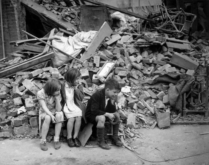 Kinder warten vor den Trümmern ihres ehemaligen Zuhauses in East London, 1940. Foto: Sue Wallace / CC BY-SA 2.0, via Wikimedia Commons