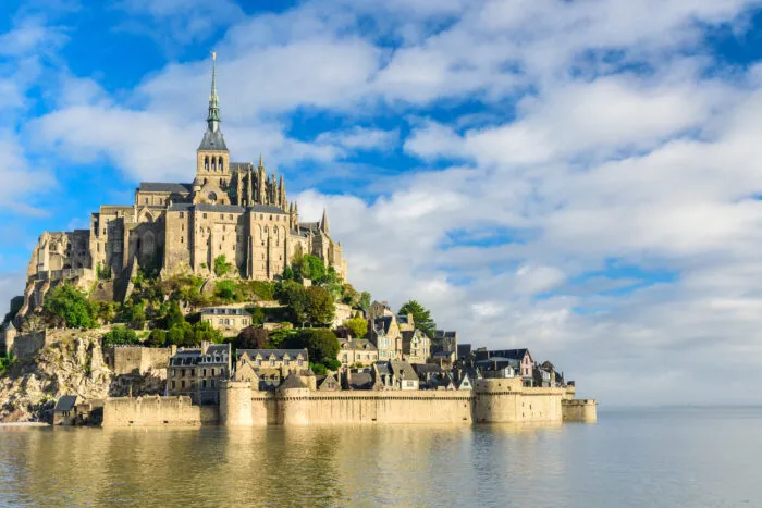 Mont-Saint-Michel bei Ebbe, wenn die Bucht ihre weiten Sandflächen freigibt. Zweimal täglich weicht das Meer und kehrt dann wieder zurück, um den Felsen zu umspülen. Ein Rhythmus, dem sich die Baumeister des Mittelalters ständig anpassen mussten. Foto: samael334/iStock