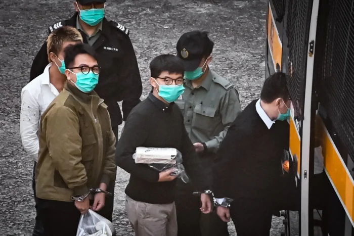 Die Aktivisten Joshua Wong (Mitte) und Ivan Lam (rechts) besteigen am 2. Dezember 2020 einen Polizeiwagen, bevor sie zu einem Gericht gebracht werden, um wegen eines Protests im Jahr 2019 vor dem Polizeipräsidium der Stadt verurteilt zu werden. Die Verhandlung fand in einer Hochsicherheitsanstalt in Hongkong statt. Foto: Anthony Wallace/AFP via Getty Images