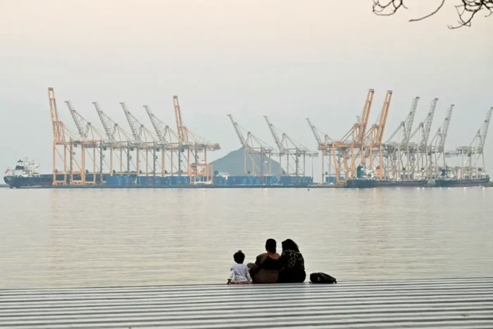 Eine Familie sitzt vor der Kulisse einer Werft vor der Küste von Fudschaira, in der Straße von Hormus in den Vereinigten Arabischen Emiraten; Aufnahme vom 25. Februar 2026. Foto: Giuseppe Cacace/AFP via Getty Images