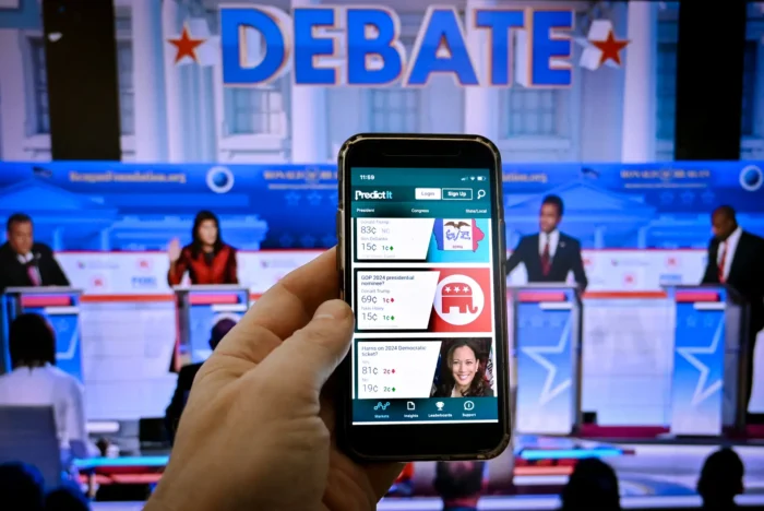 Diese Fotomontage, aufgenommen am 1. November 2023 in Washington, zeigt den Bildschirm eines Smartphones mit der Online-Wahlprognoseplattform PredictIt und einem Bild der zweiten Vorwahldebatte der Republikaner in Simi Valley, Kalifornien, am 27. September 2023. Wähler, die sich über wichtige Wahlen informieren und den Kontext verstehen möchten, nutzen zunehmend die Prognosen von Wahlprognoseplattformen, bevor sie ihre Stimme abgeben. Foto: Olivier Douliery/AFP via Getty Images